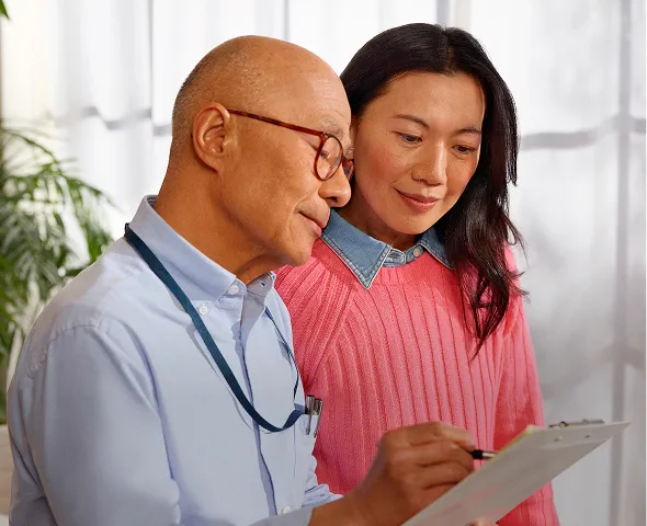 Fictional caregiver talking to her fictional patient in a bright consultation room about KISQALI® for breast cancer